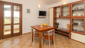 Un coin repas avec une table et des chaises en bois, un téléviseur fixé au mur et une vitrine avec des étagères.