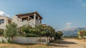 Une maison à deux étages avec un balcon, entourée de verdure et sous un ciel dégagé.
