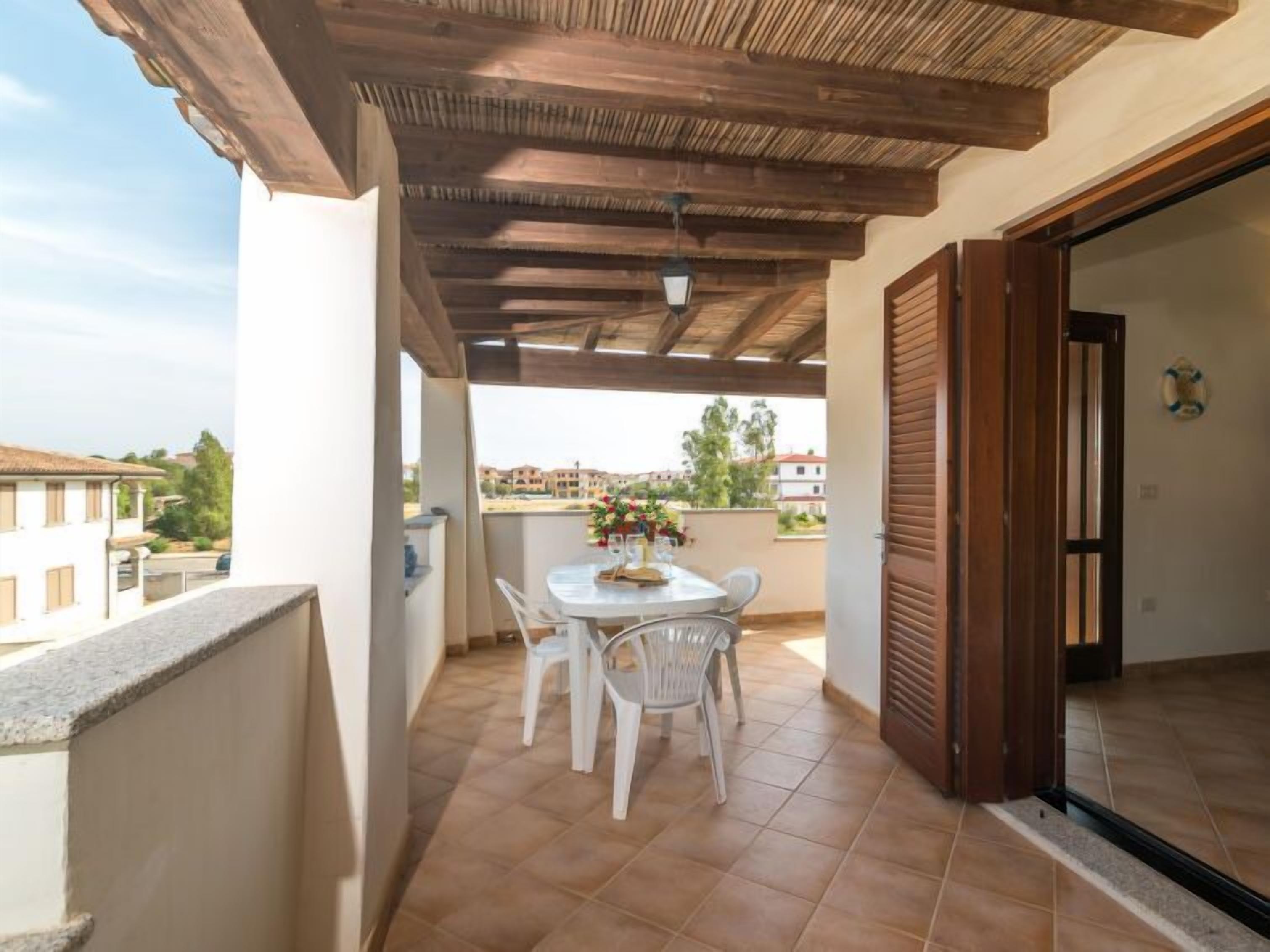 A covered outdoor patio with a table and chairs, a view of the neighborhood, and a wooden ceiling.