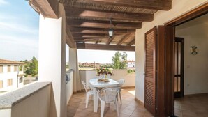 Une terrasse extérieure couverte, dotée d’une table et de chaises, offrant une vue sur le quartier et agrémentée d’un plafond en bois.