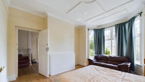A bedroom with a large bed, a window with curtains, a brown leather sofa, and a staircase leading to another room.