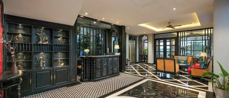 A spacious lobby with a black and white patterned floor, a central decorative element, and a seating area with wicker furniture.