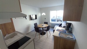 Een compacte keuken met een eethoek, een koffieapparaat en een televisie aan de muur.