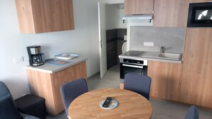 Een praktische keuken met een magnetron, fornuis en koffiezetapparaat. Er is een zithoekje met een ronde tafel en twee stoelen.