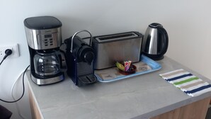 Een keuken met een koffiezetapparaat, broodrooster, waterkoker, en een blauwe dienblad met een gestreepte doek.