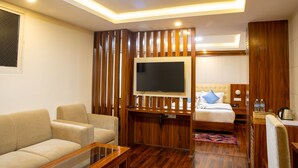 A modern hotel room with a flat-screen TV, a sofa, a bed with a headboard, and wooden paneling. - HOTEL DREAMS CONNECT (Kathmandu)