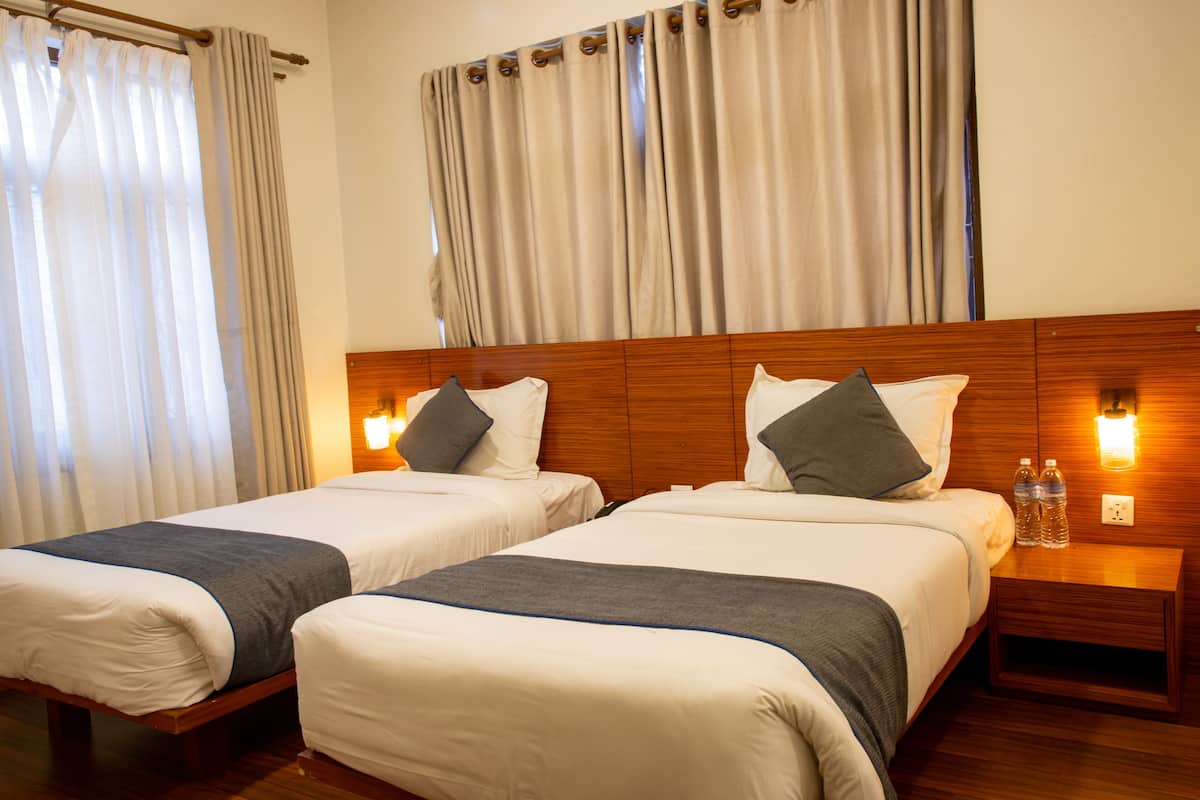 A hotel room with two beds, wooden headboards, bedside tables, and curtains.