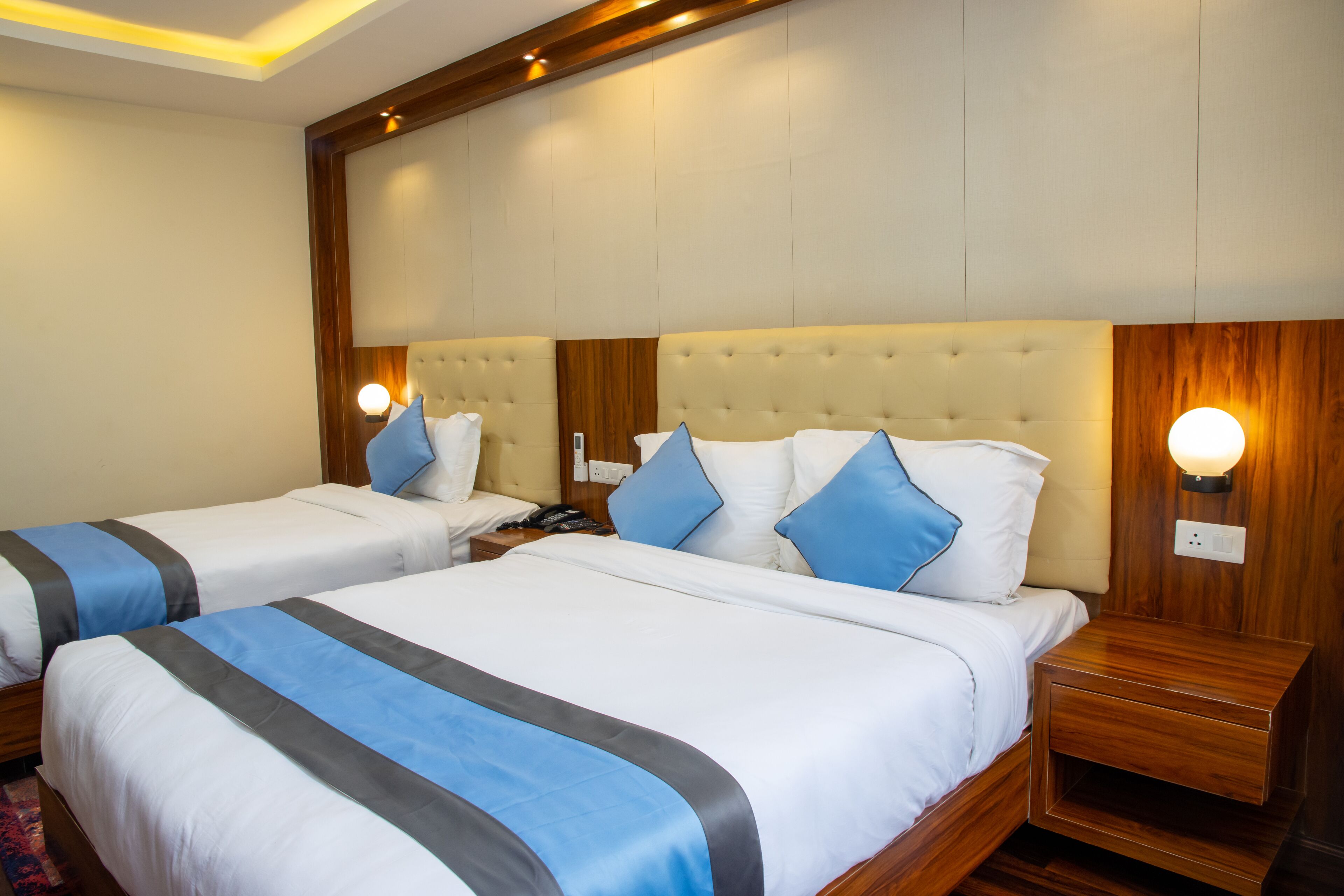 A hotel room with two beds, each with a headboard, bedside tables, and wall-mounted lamps.