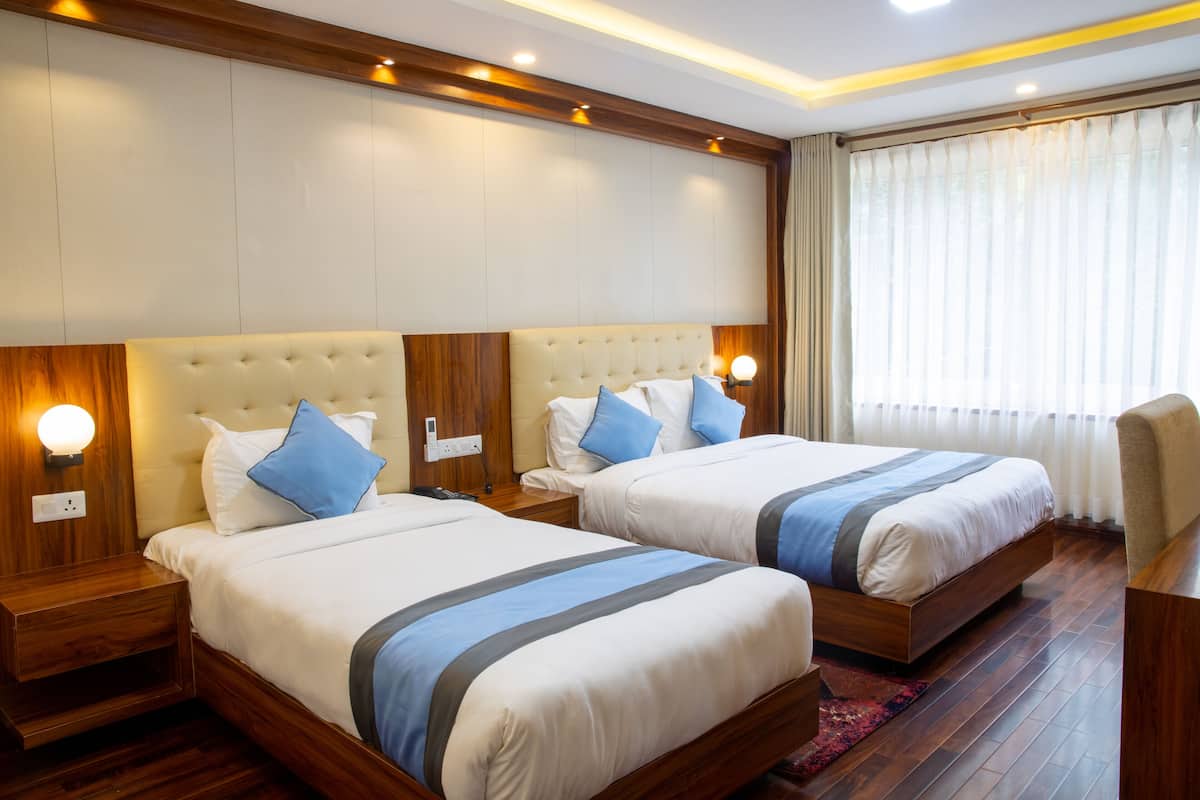 A hotel room with two beds, wooden headboards, bedside lamps, and a large window with curtains.