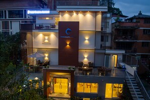 Um hotel moderno com um logotipo em destaque, área de estar externa e uma entrada bem iluminada.