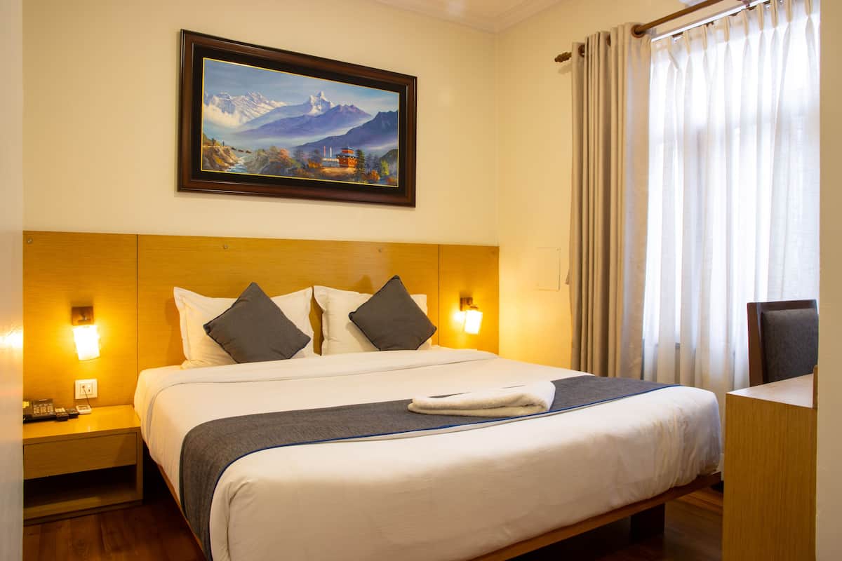 A hotel room with a large bed, two bedside tables, a desk, and a painting on the wall.