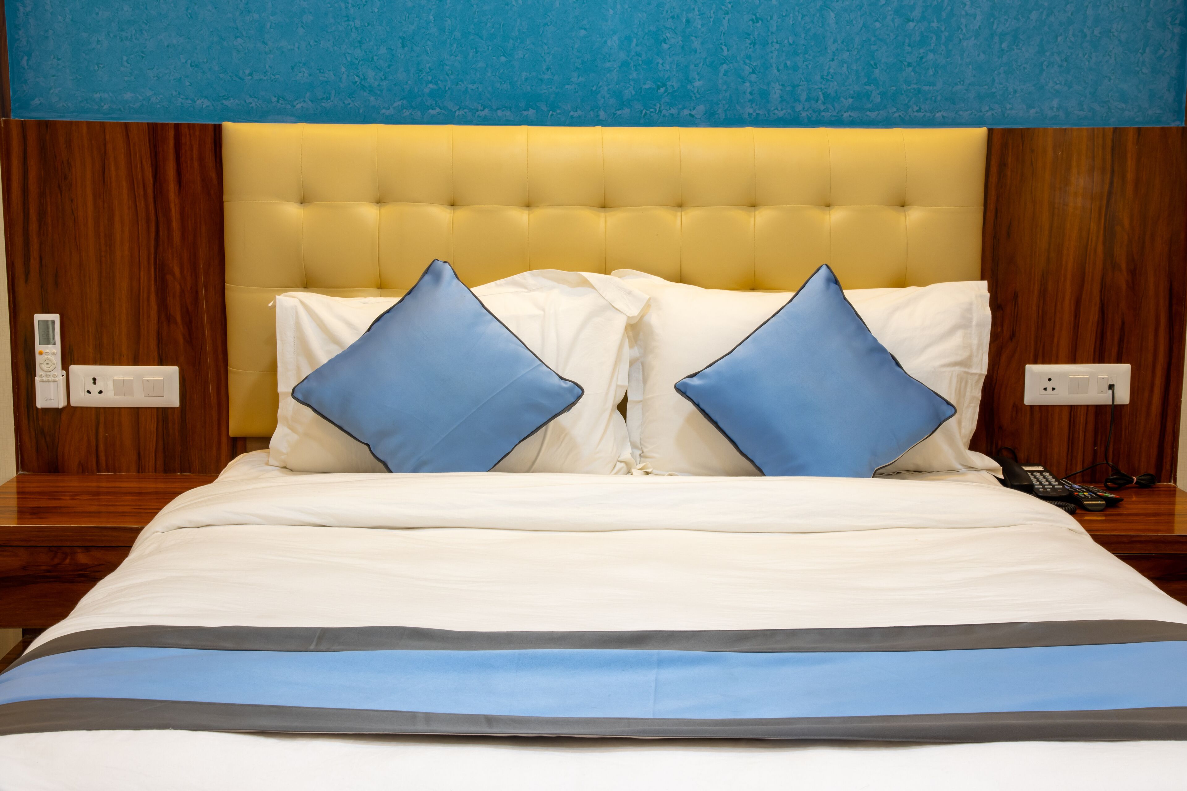 A hotel room with a large bed, two blue pillows, a white comforter, and a wooden headboard.