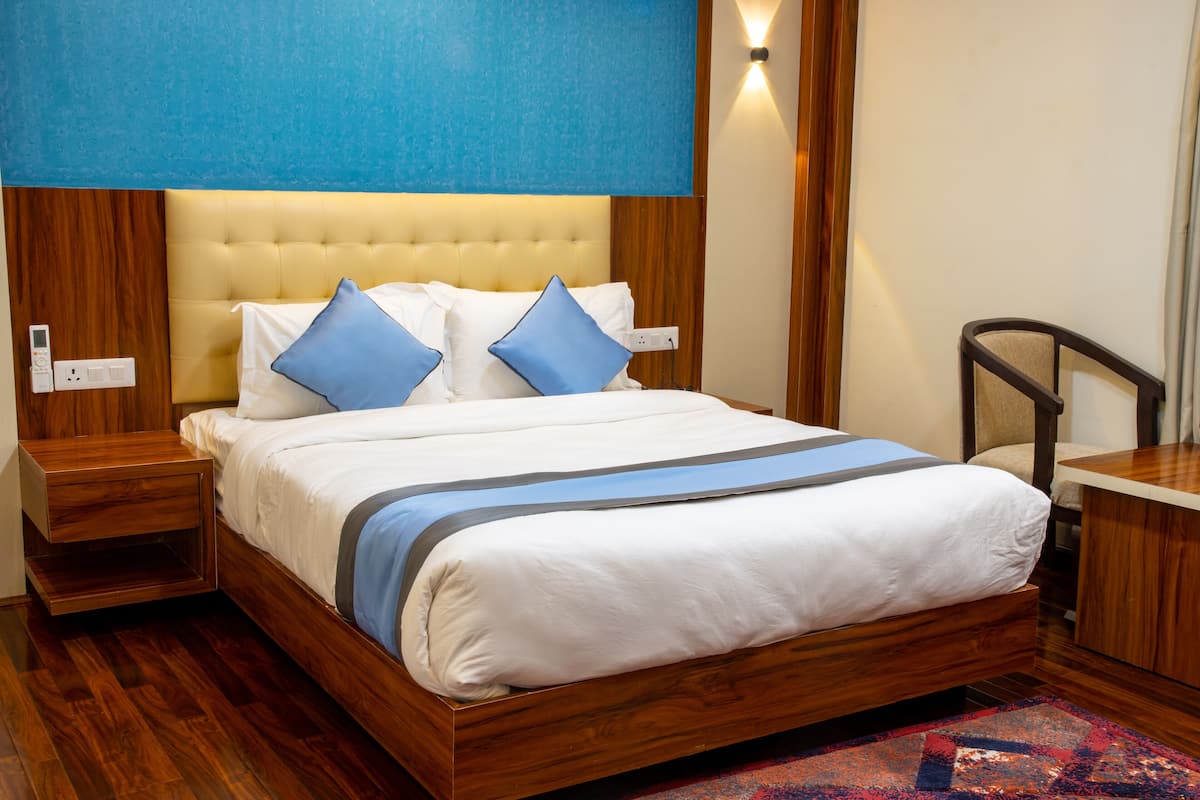 A neatly made bed with a headboard, a wooden nightstand, and a desk with a chair.