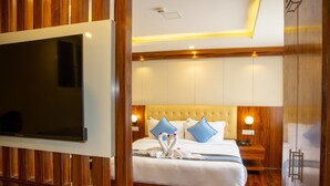 A hotel room with a large flat-screen TV, a bed with white bedding and blue pillows, wooden paneling, and a wooden wardrobe. - HOTEL DREAMS CONNECT (Kathmandu)