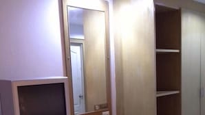 A compact room with a television on a wooden stand, a small refrigerator, a wooden chair, and a wardrobe with shelves. - Vech guesthouse2 (Patong)