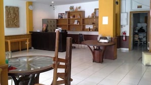A hotel lobby with a reception desk, a round table with chairs, and a bookshelf with framed pictures. - Vech guesthouse2 (Patong)