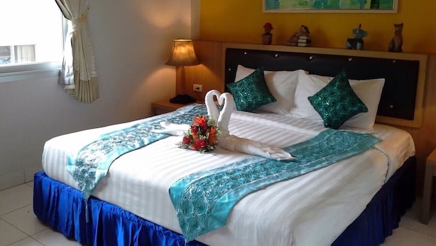 A neatly made bed with a swan-shaped pillow and decorative pillows, a blue and white bedspread, and a colorful painting on the wall. - Vech guesthouse2 (Patong)