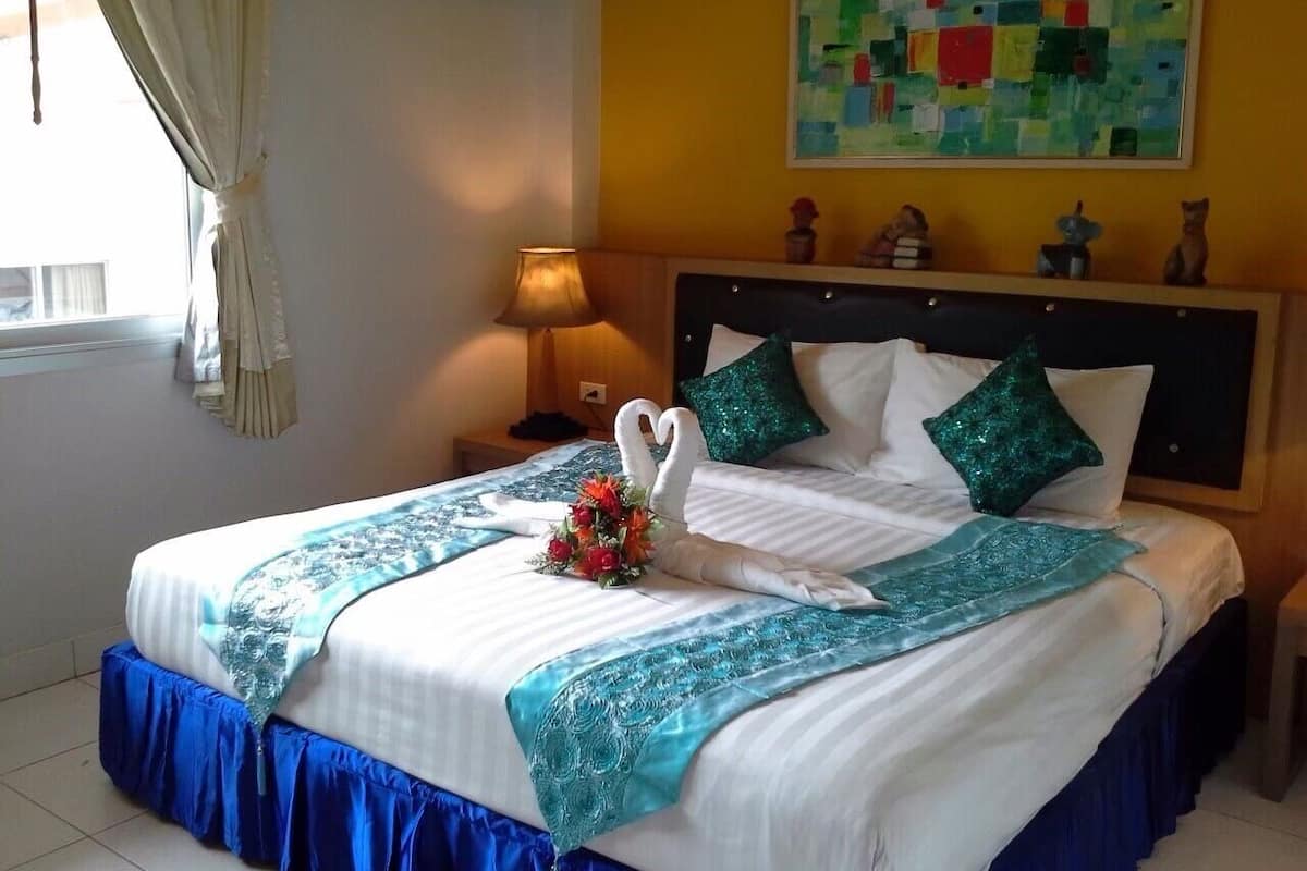 A neatly made bed with a swan-shaped pillow and decorative pillows, a blue and white bedspread, and a colorful painting on the wall.