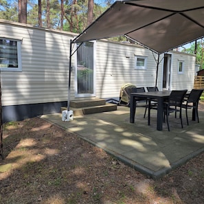 Een overdekt terras met een tafel, stoelen, een barbecue en een kleine hond.