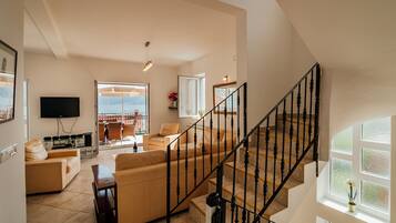 A spacious living room with a large sofa, a TV mounted on the wall, and a staircase with a black railing.
