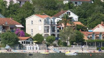 A coastal building with a balcony, surrounded by trees and a beach.