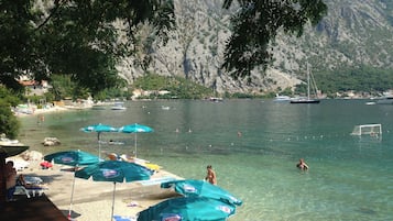 A beach with clear water, umbrellas, and boats.