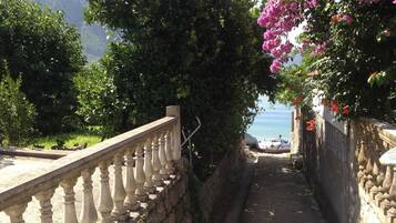 A stone pathway with balustrades, leading to a body of water, surrounded by greenery and mountains.