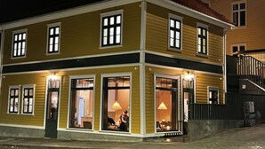 Ein zweistöckiges Gebäude mit gelber Fassade, großen Fenstern und einem sichtbaren Essbereich mit einer Lampe.