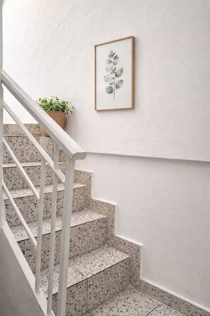 Eine Treppe mit weißen Geländern und gefleckten Stufen, ein gerahmtes Pflanzenbild an der Wand und ein Blumentopf im Treppenabsatz.