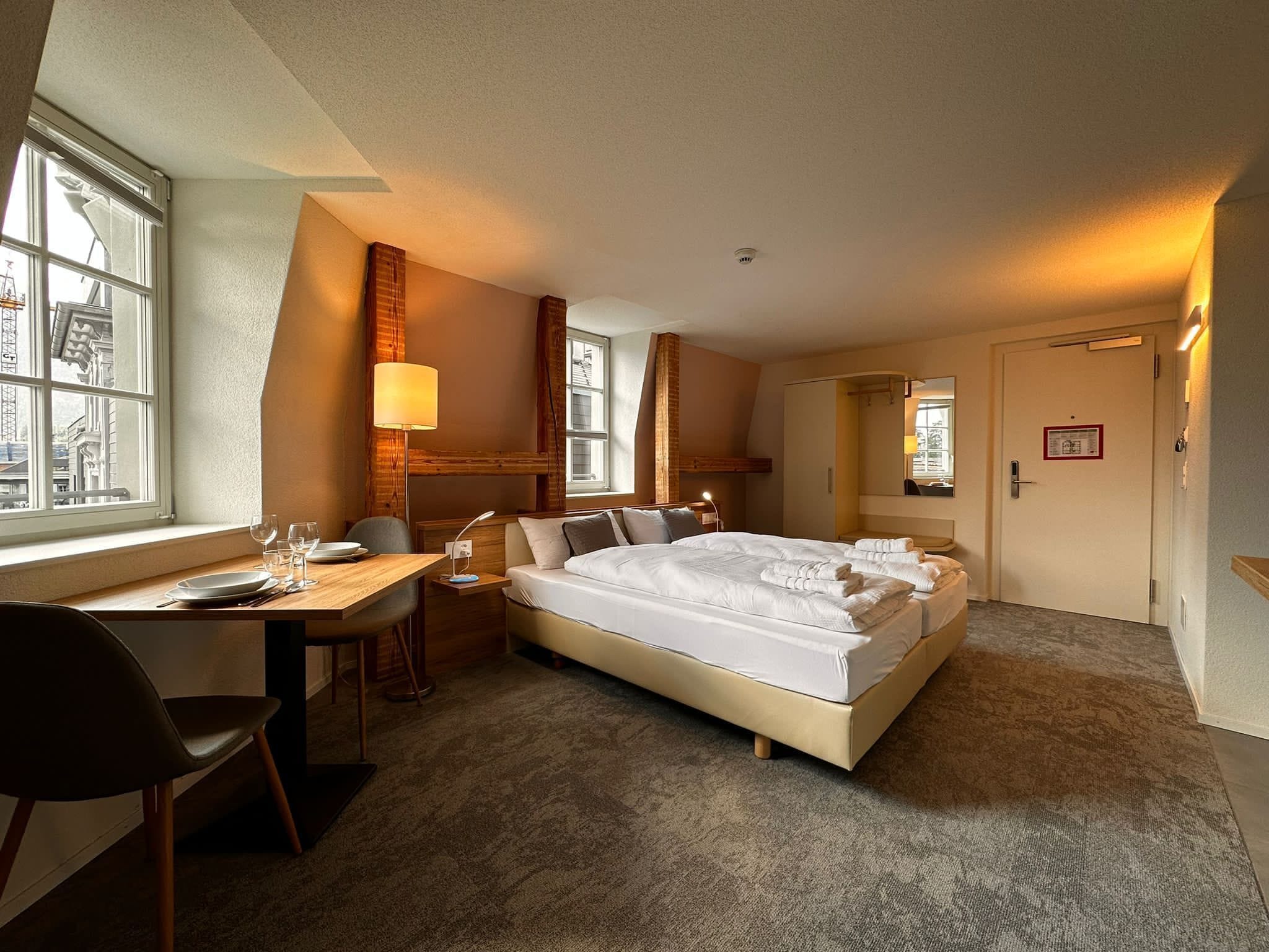Une chambre d’hôtel avec un lit, un bureau et une chaise. Il y a une fenêtre et une porte.