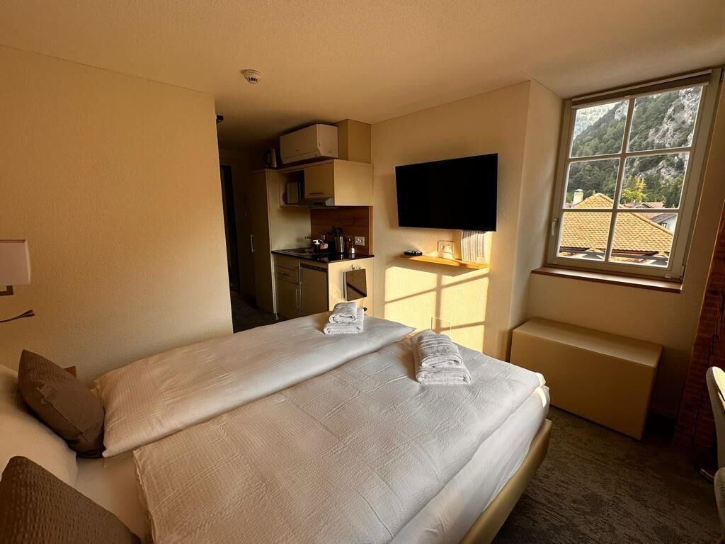 Une chambre d’hôtel avec un grand lit, un téléviseur fixé au mur et une fenêtre donnant sur une vue sur la montagne.