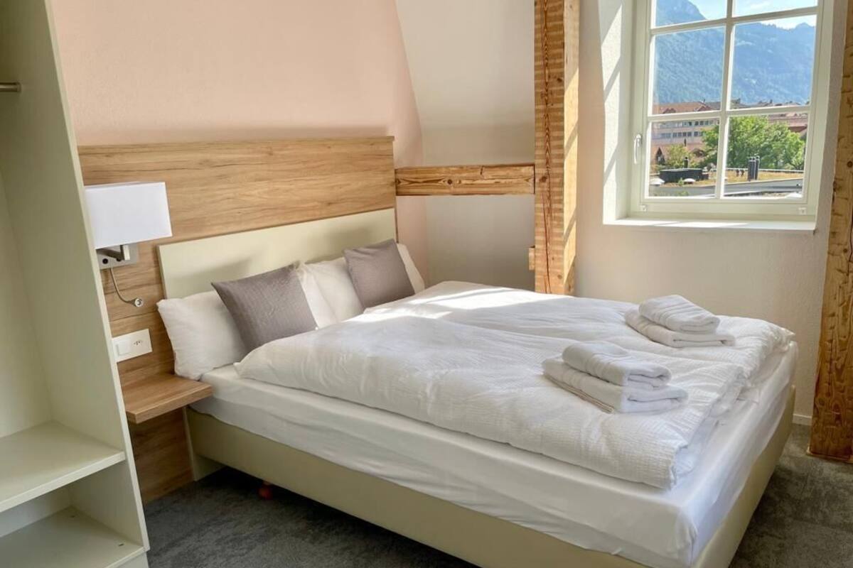 A neatly made bed with folded towels, a bedside lamp, and a view of mountains through a window.