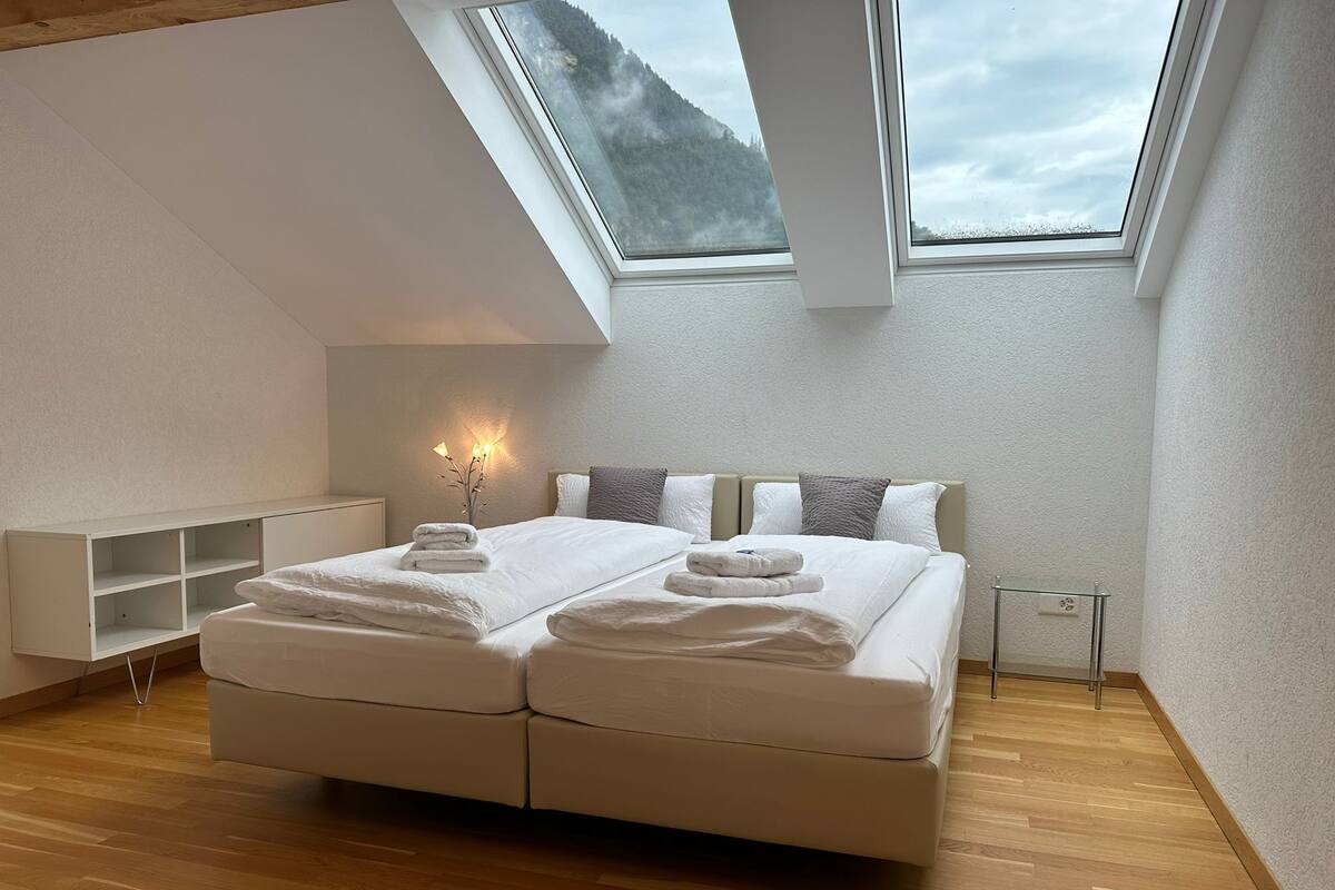 A modern bedroom with a skylight, a bed with towels, and a bedside table.