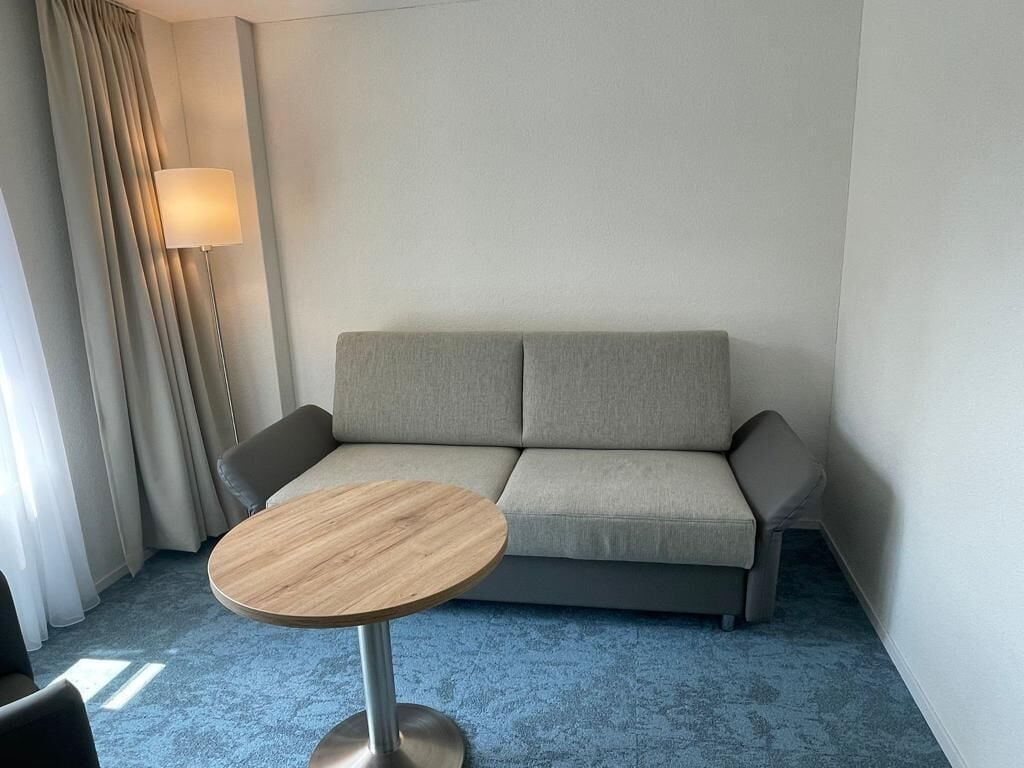 Une pièce avec un canapé gris, une table ronde en bois et une lampe.