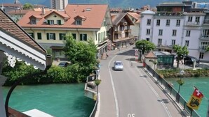 Vista da un balcone su una strada con edifici, un fiume e montagne sullo sfondo.