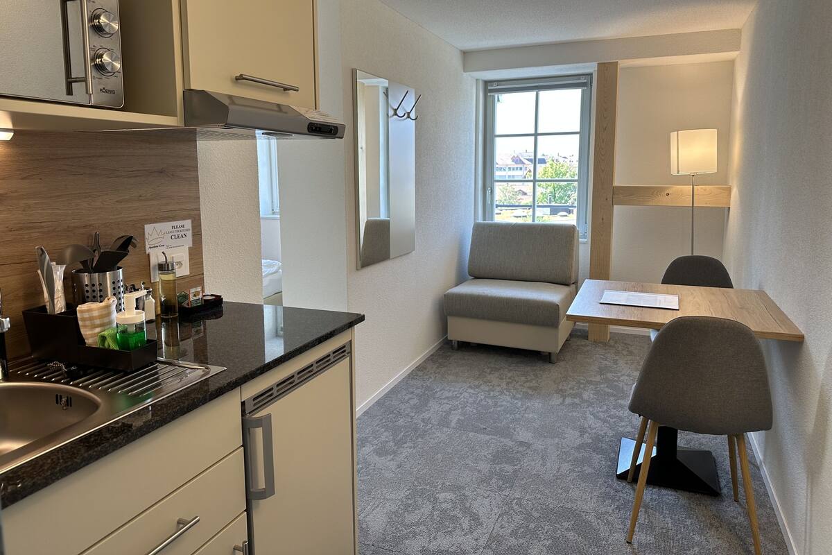 A compact kitchen with a sink, countertop, and a small dining area with a chair and table.
