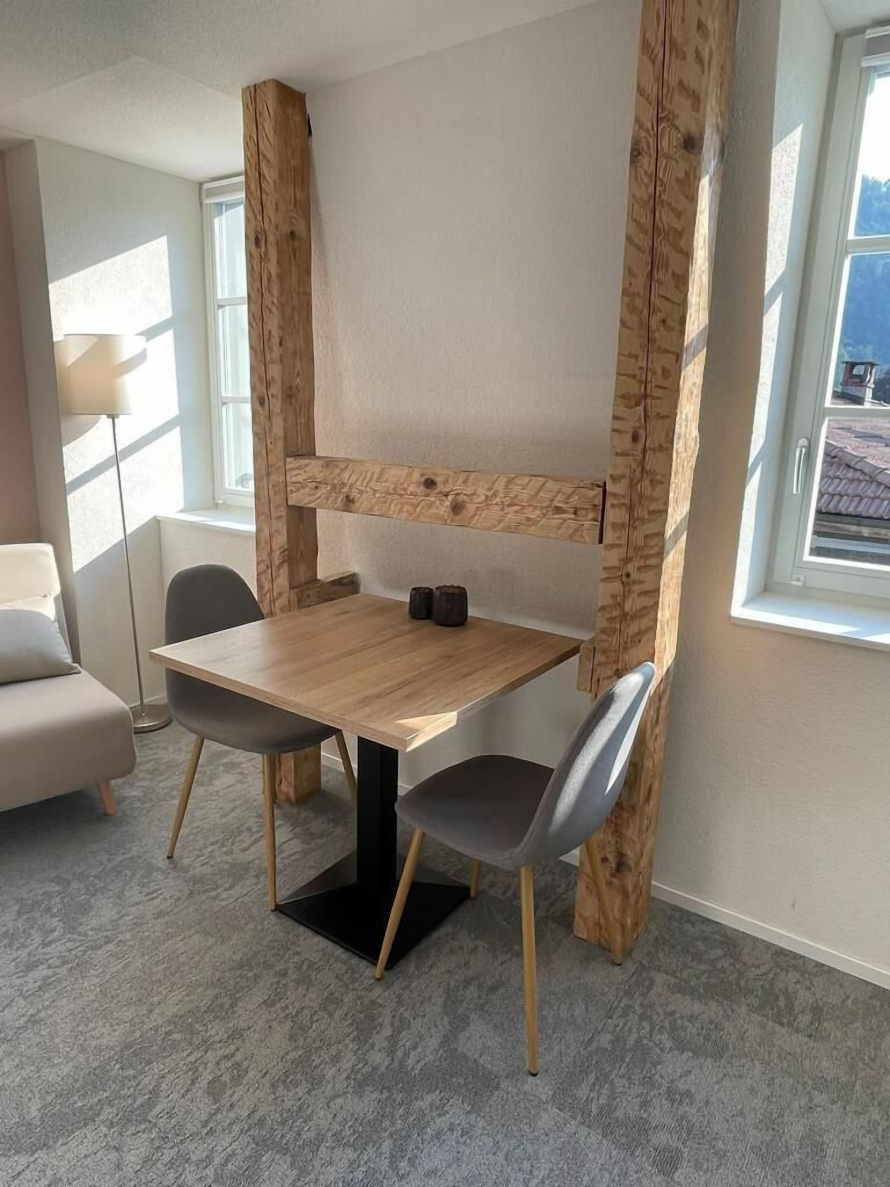 A compact room with a wooden table and two chairs, a sofa, and a floor lamp.