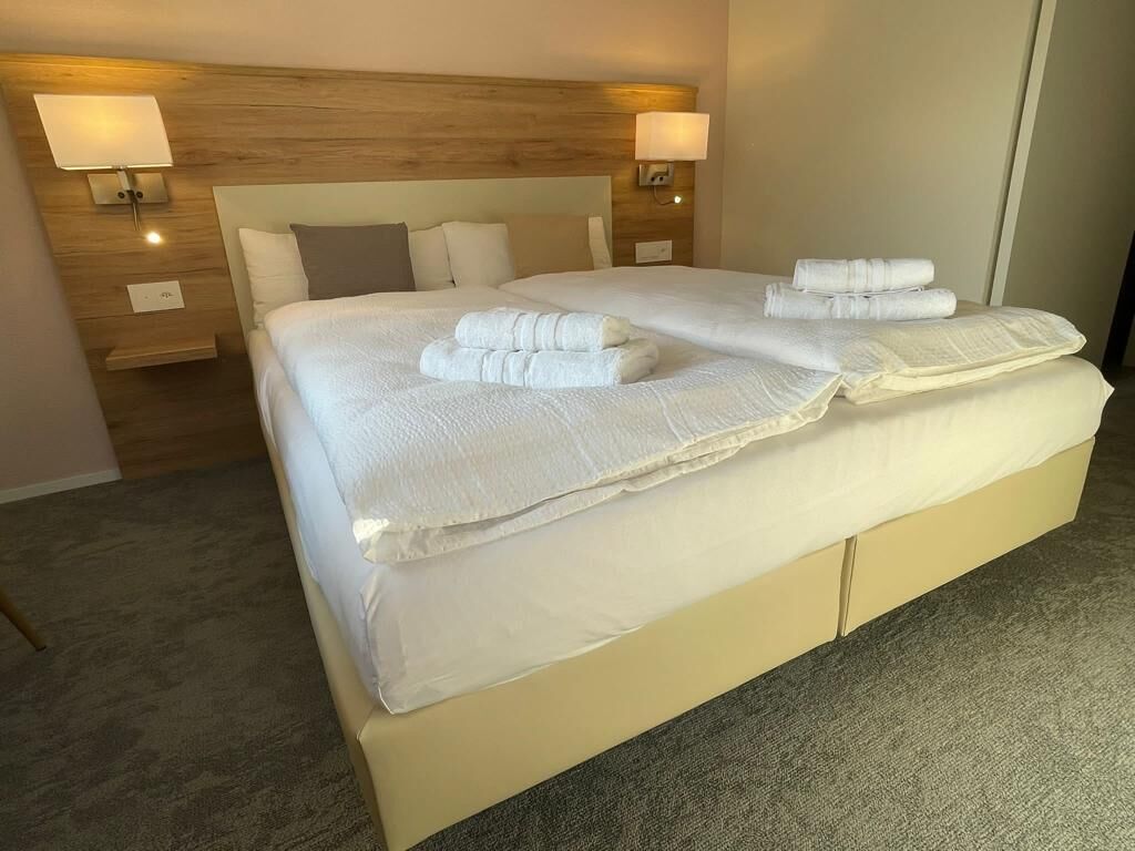 A double bed with white linens, two bedside lamps, and a wooden headboard.