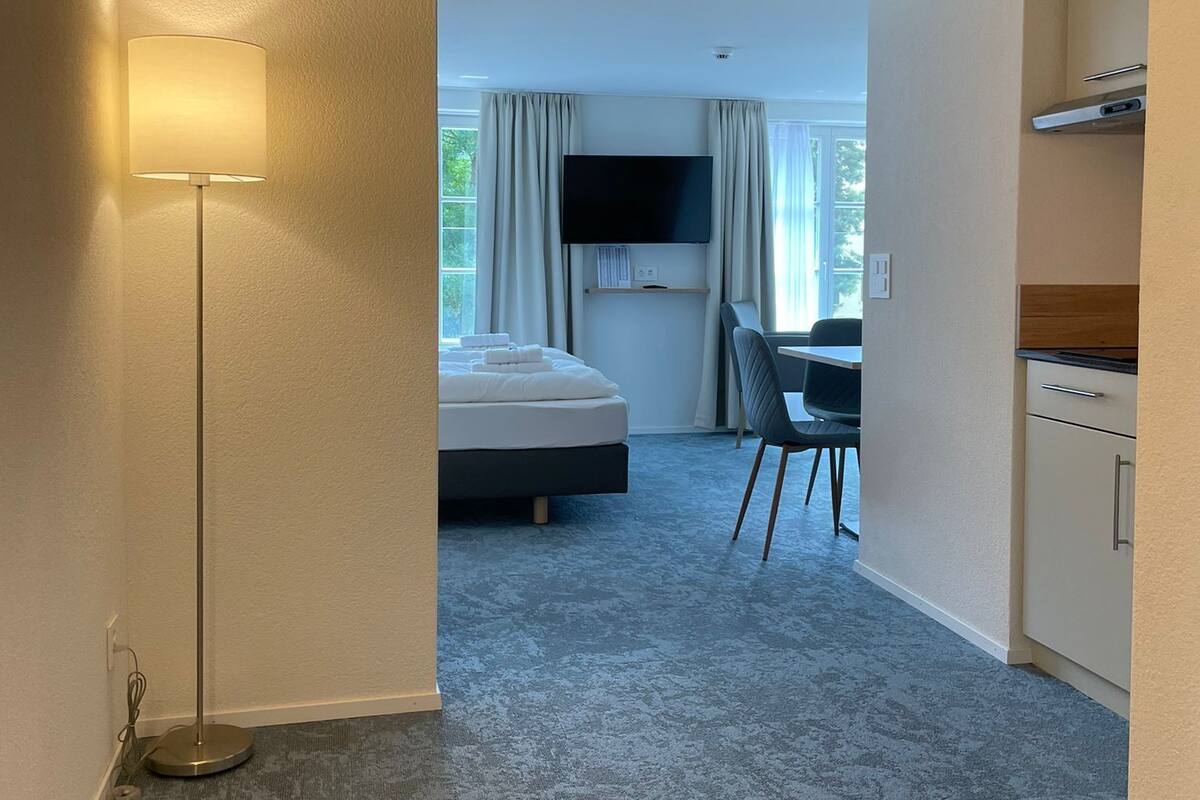 A hotel room with a bed, a desk, a chair, a TV, and a lamp.
