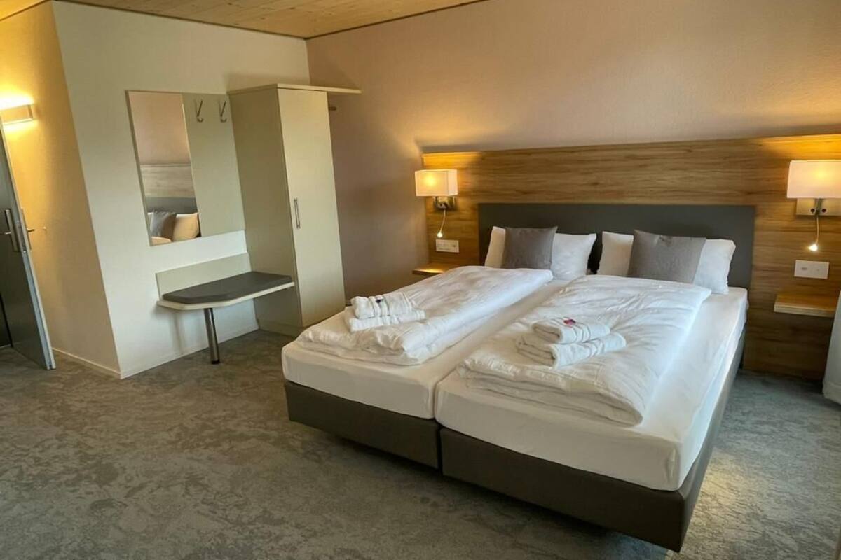 A double bed with a wooden headboard, two bedside tables with lamps, a mirror, and a built-in bench.