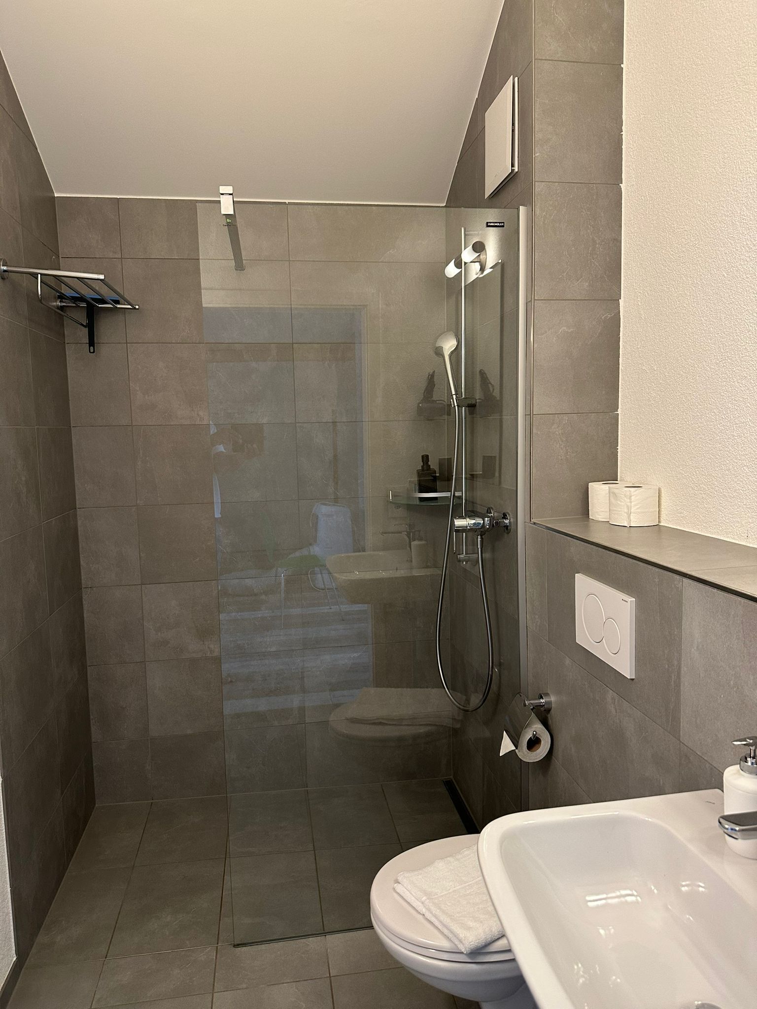 Un baño moderno con ducha de vidrio, lavamanos blanco y retrete.