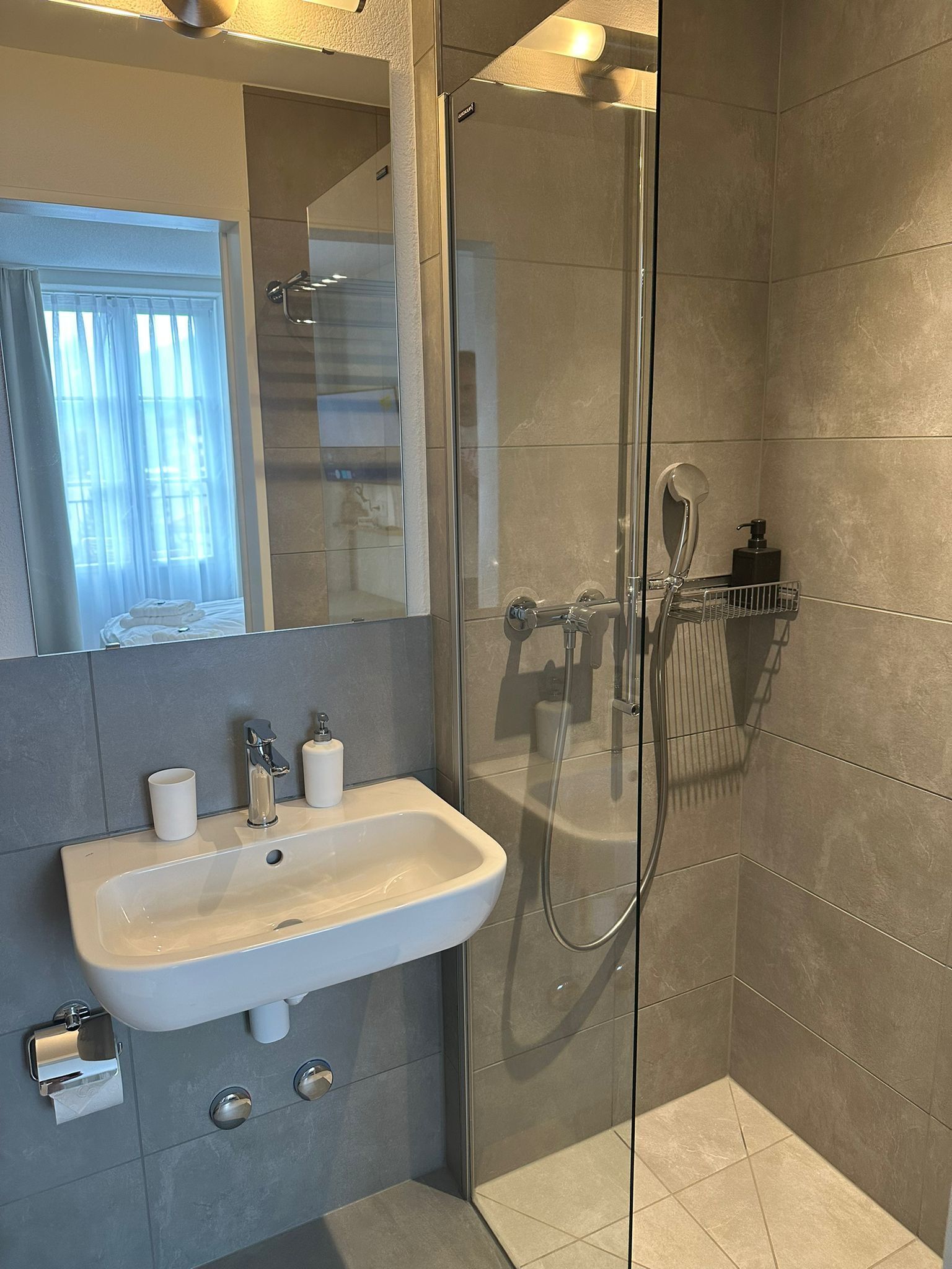A modern bathroom with a glass-enclosed shower, a white sink, and a mirror above it.