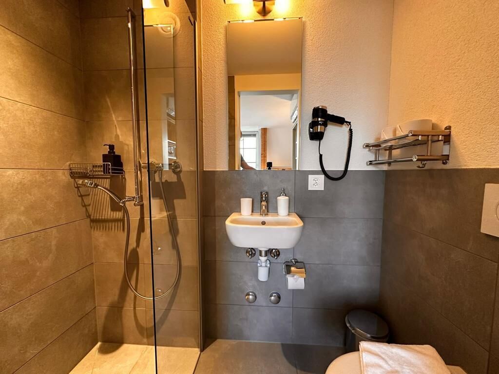 A modern bathroom with a glass-enclosed shower, a sink with a mirror above it, and a hairdryer mounted on the wall.