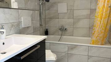 Un bany modern amb un lavabo blanc, un armari negre i una banyera.