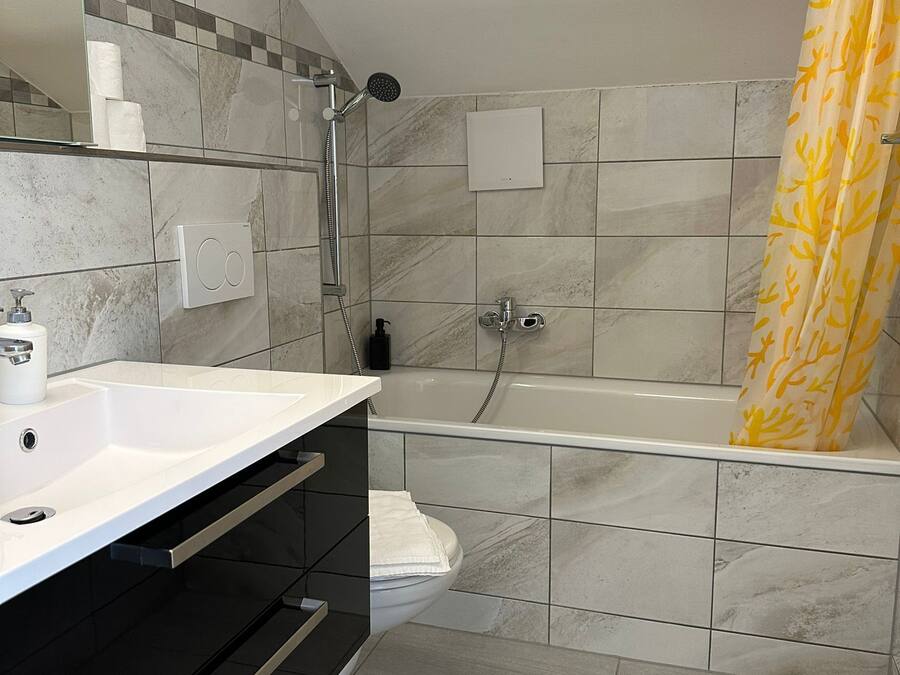 Un bany modern amb un lavabo blanc, un armari negre i una banyera.