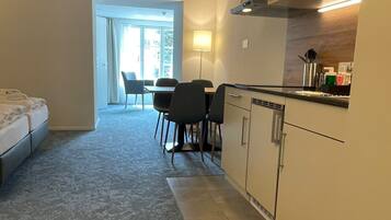 A compact hotel room with a kitchenette, a dining area with chairs, and a large window.