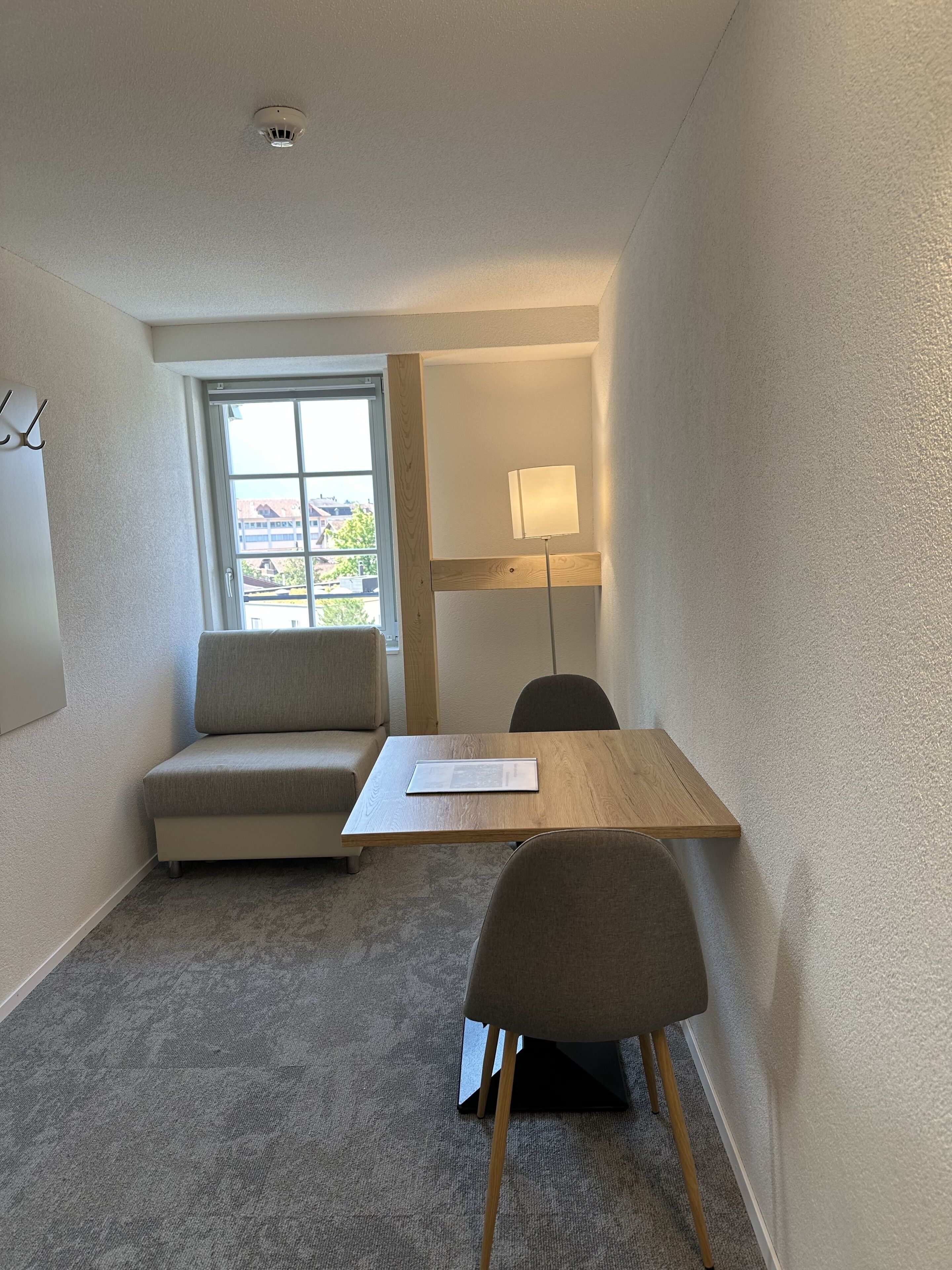 Ein kleiner, moderner Raum mit Holztisch, grauem Sofa und einer Lampe.