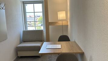 Ein kleiner, moderner Raum mit Holztisch, grauem Sofa und einer Lampe.