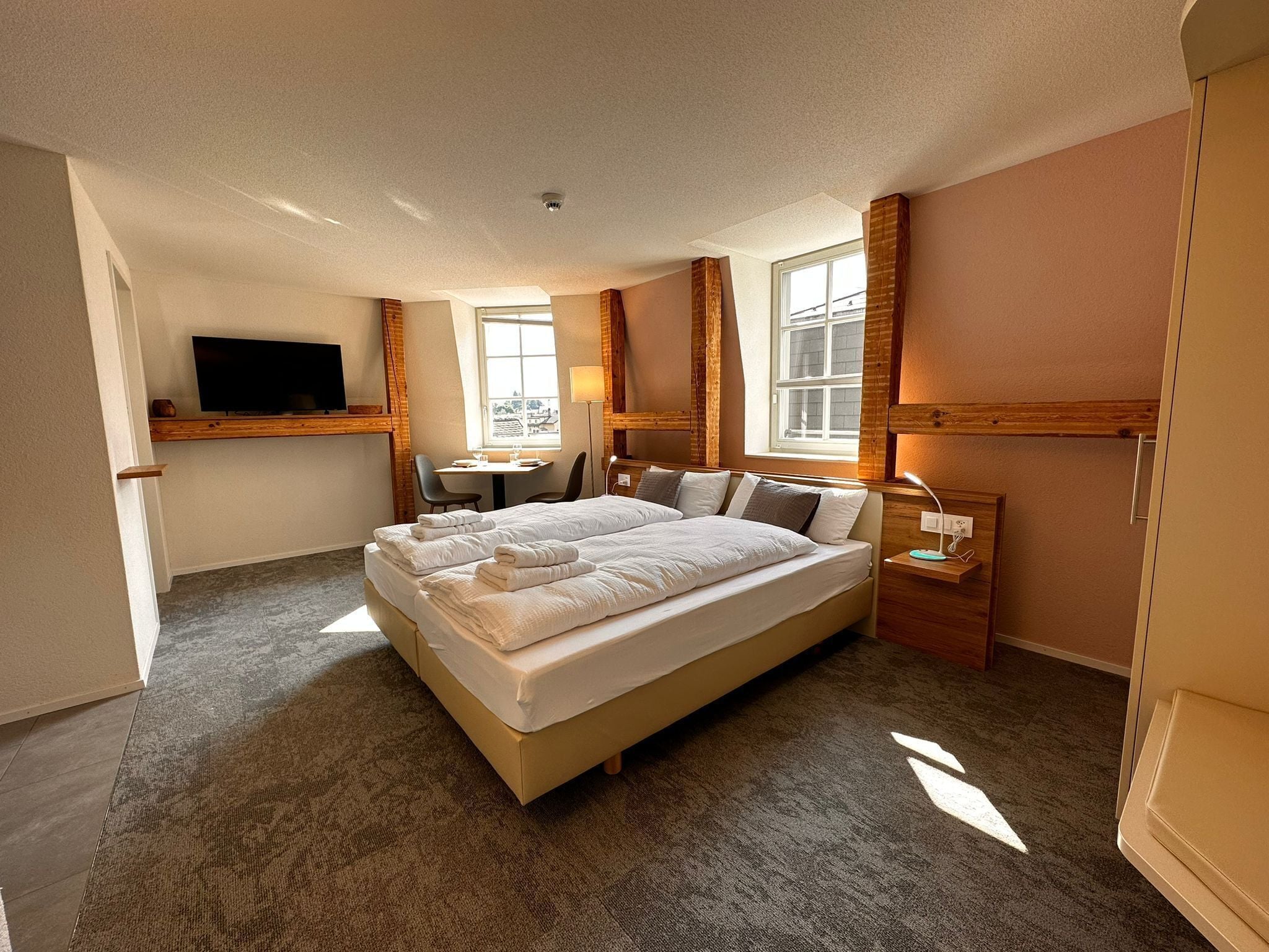 A hotel room with a large bed, a desk, a chair, a TV, and a window.