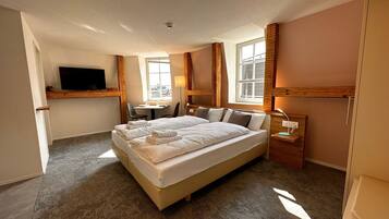 A hotel room with a large bed, a desk, a chair, a TV, and a window.